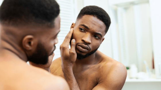 A man looks in the mirror while touching his face