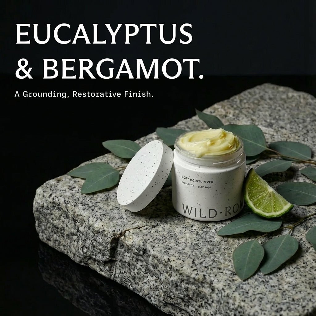 Jar of Wild Roman tallow body moisturizer with eucalyptus leaves and a bergamot on a stone surface.