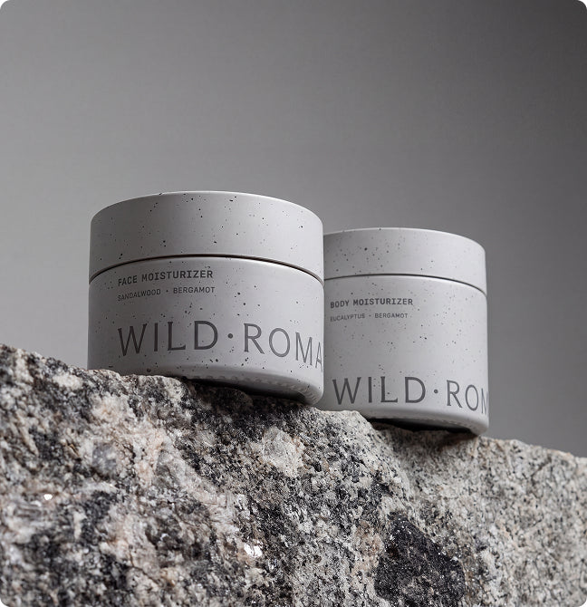 Two jars of Wild Roman body moisturizer resting on a granite rock