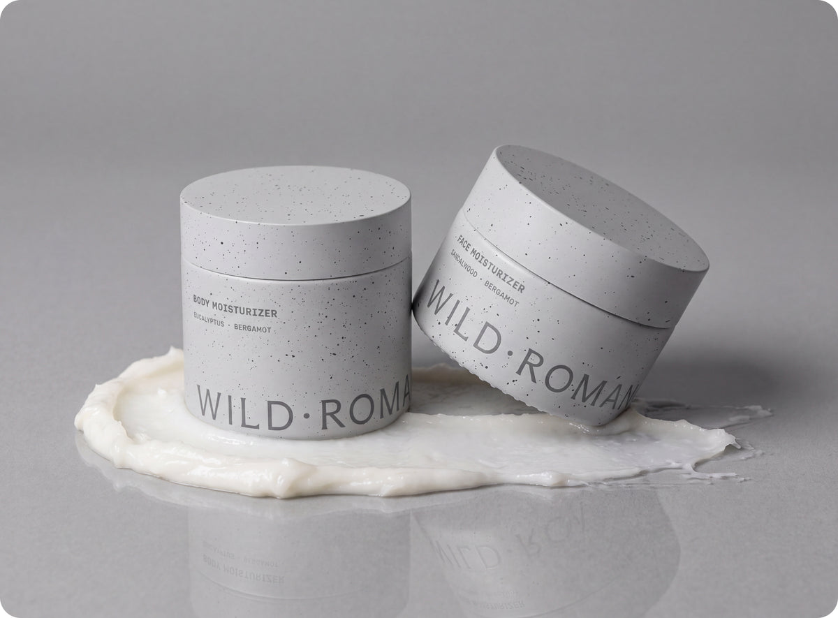 Wild Roman Body Moisturizer and Face Moisturizer jars sitting in a swirl of white cream