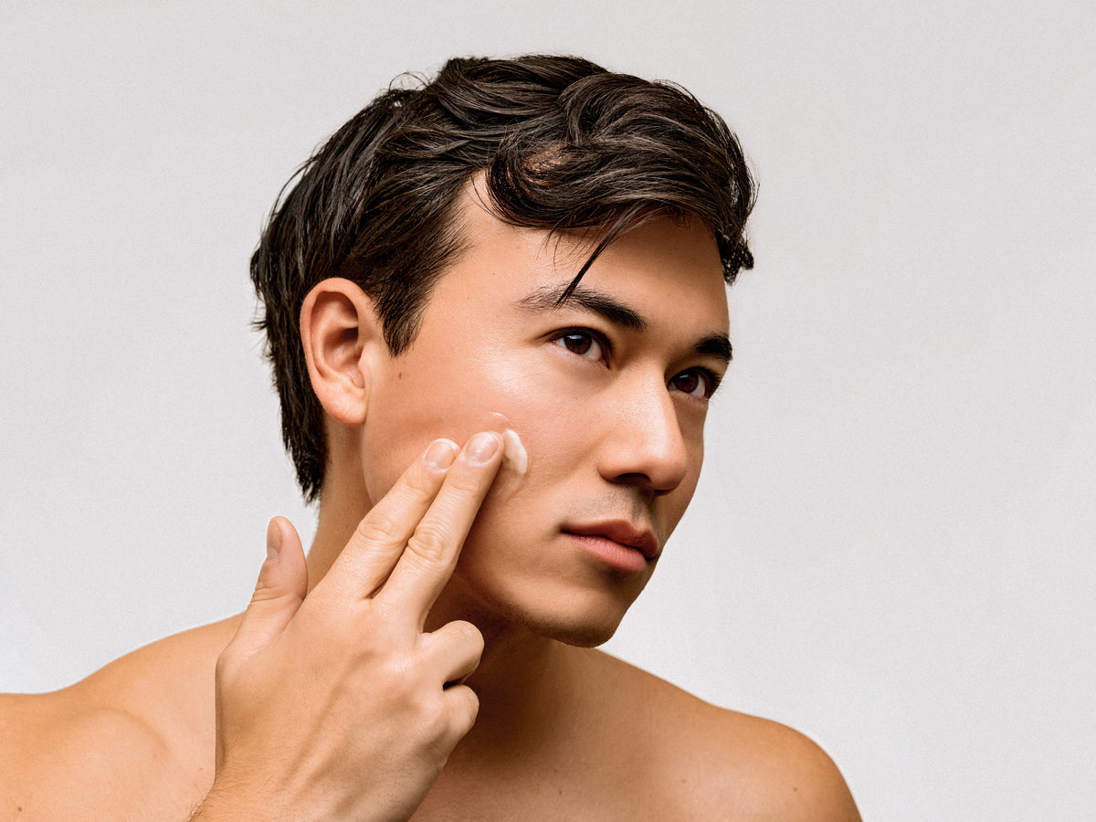 Man applying tallow cream to his face with a neutral background
