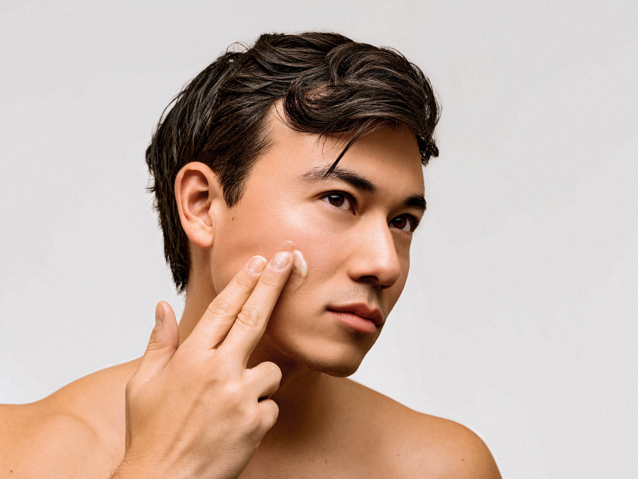Man applying tallow cream to his face with a neutral background